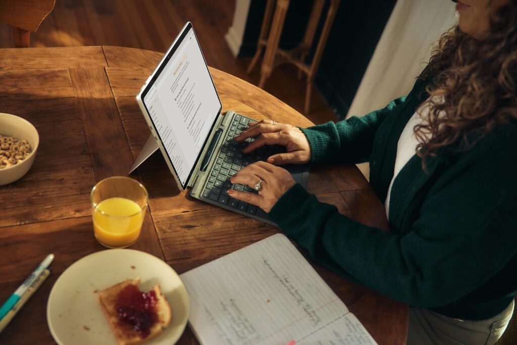Woman typing on laptop at wooden table with breakfast