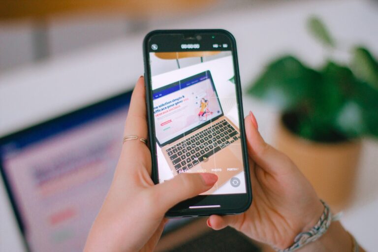 A person holding a cell phone in front of a laptop