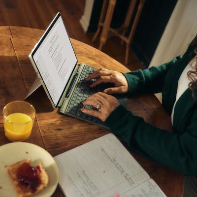 Woman typing on laptop at wooden table with breakfast