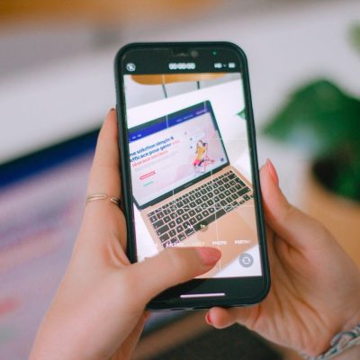 A person holding a cell phone in front of a laptop